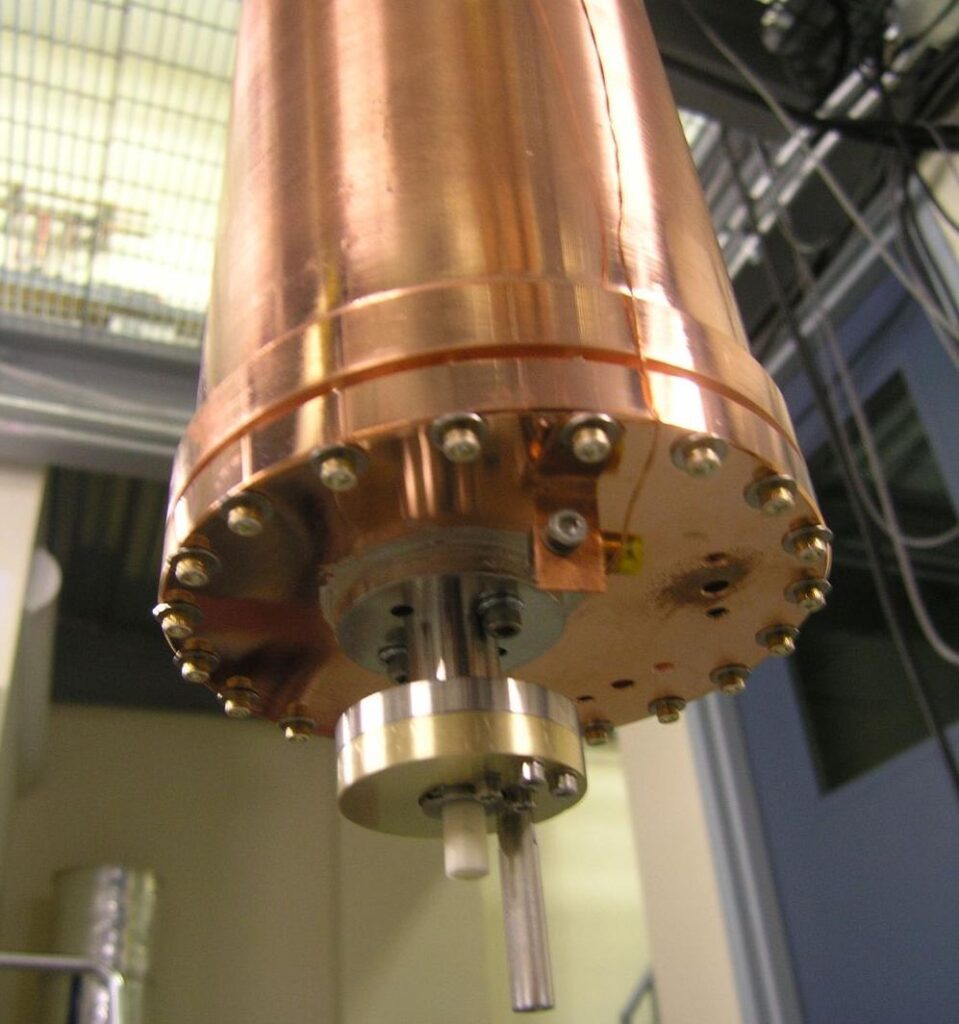 The HAYSTAC microwave cavity: a shiny copper cylinder about 4" in diameter and 10" tall, viewed from below