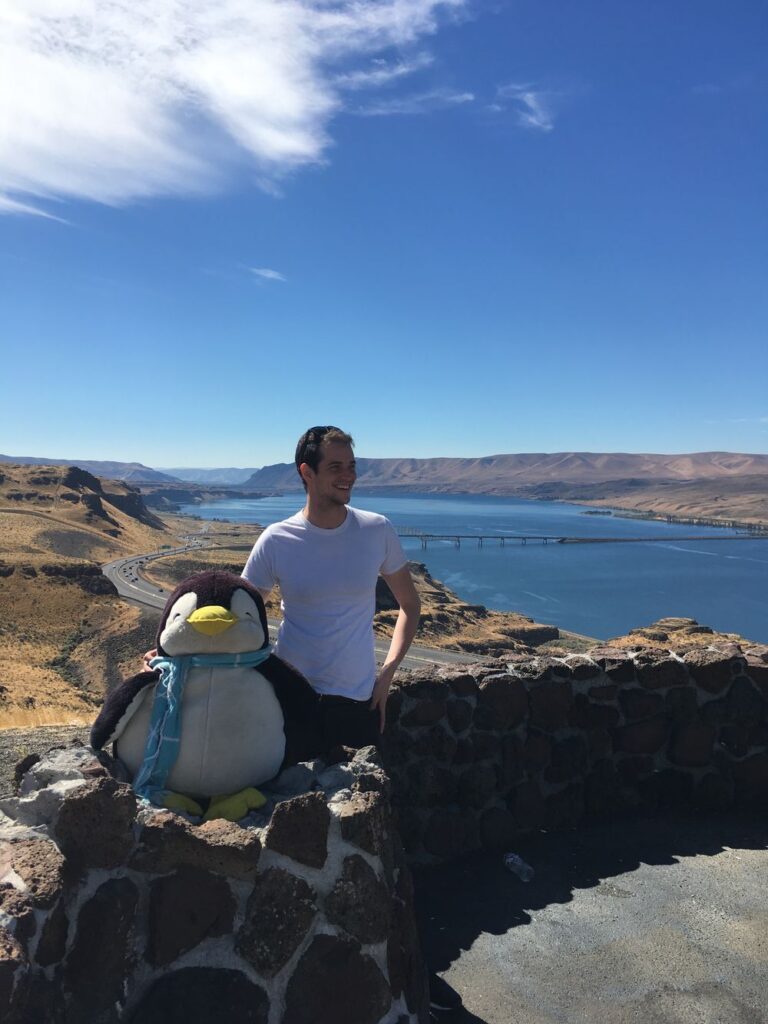 Ben and his stuffed penguin Pembroke (who's about 2 feet tall) on a cross-country road trip, at a rest stop overlooking the Columbia River.