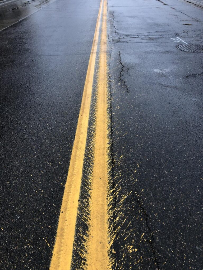 Double yellow lines in the middle of a street in Boulder. One is perfectly clean the other has splatter all over the place.