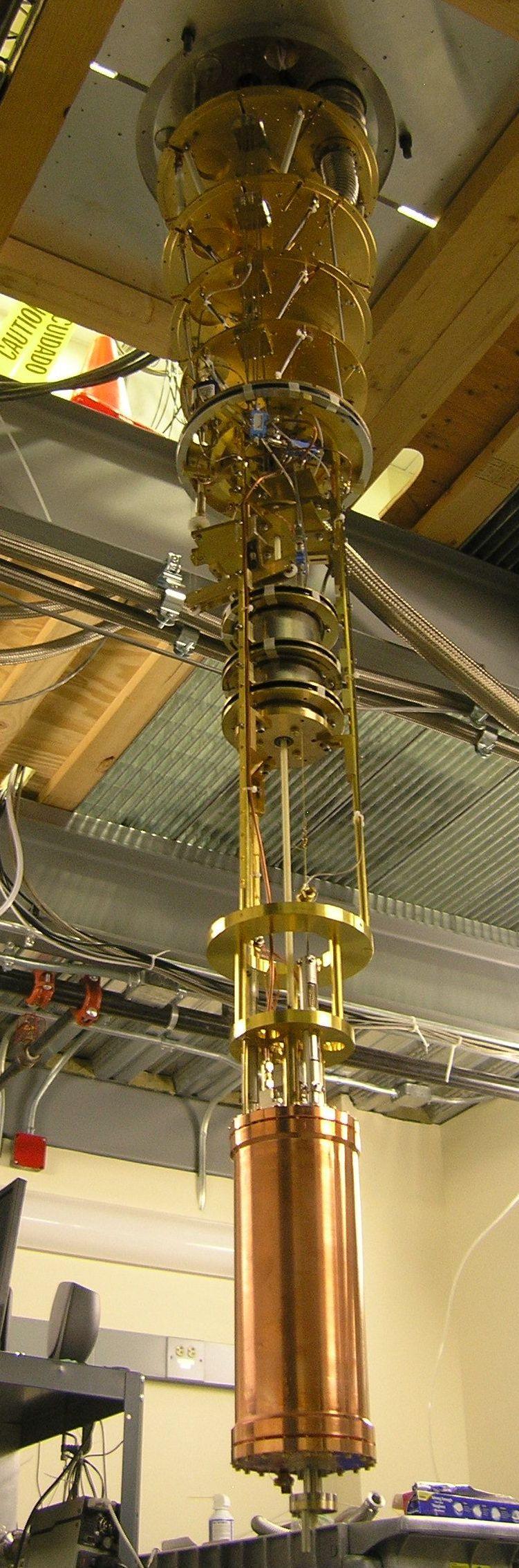 The HAYSTAC detector before it is enclosed in thermal shielding and inserted into the magnet. The cavity hangs from a long gold-plated support structure attached to the base plate of the dilution refrigerator, a stack of five gold plates hanging from the ceiling of the lab.